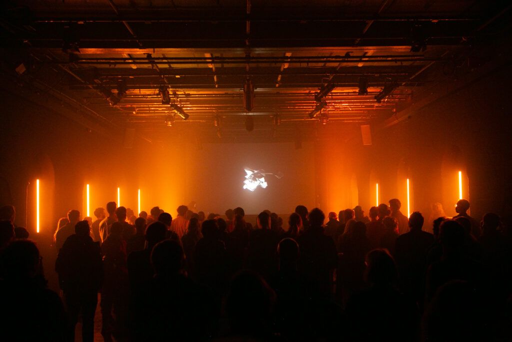 A crowd of people at Sonica 2022. Orange lights light up the crowd.