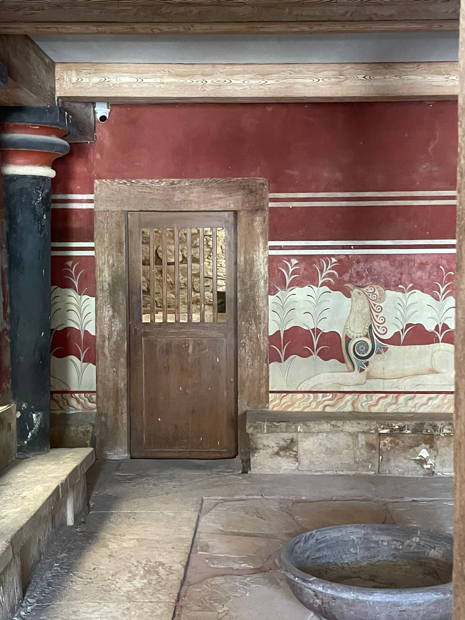 A stone building with ornate wall paintings of mythical animals and thick wooden doors and beams.